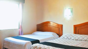 A hotel room with two single beds, a window with curtains, an air conditioning unit, and a wall-mounted light.