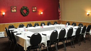 Une salle de conférence avec une longue table, des chaises noires et un mur rouge orné de deux guirlandes et de deux appliques murales.