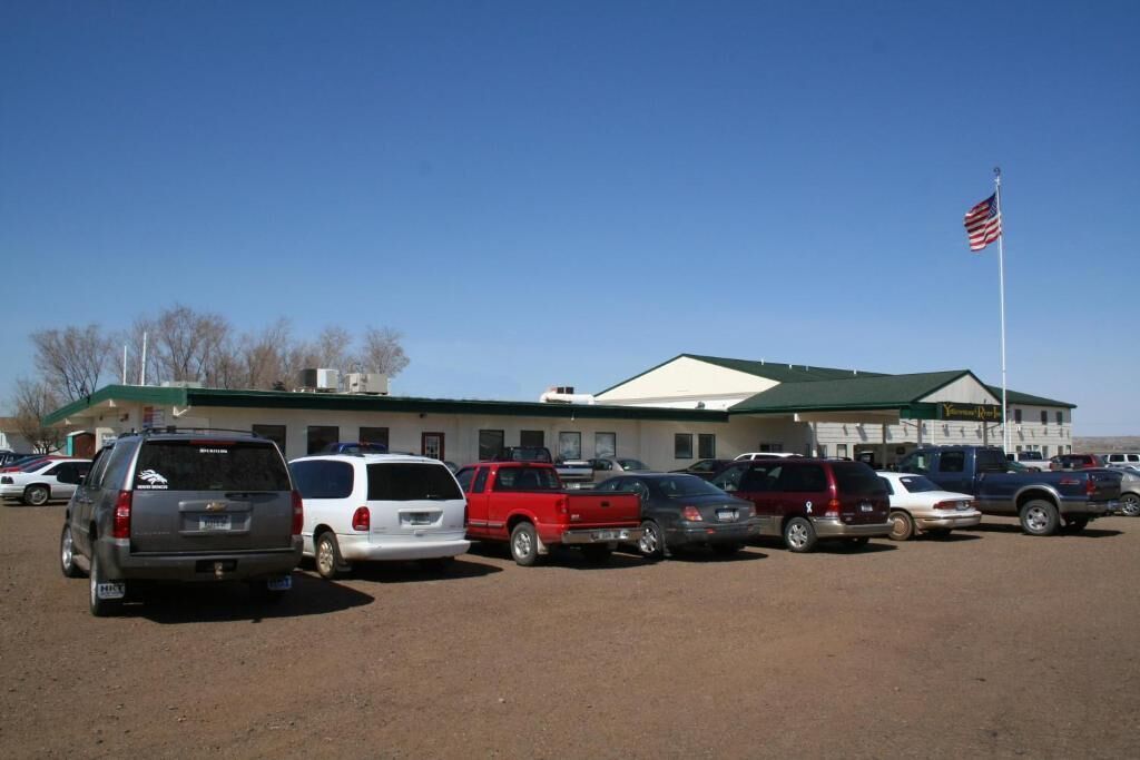 A parking lot with several vehicles, a building with a green roof, and an American flag.