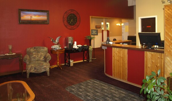A reception area with a wooden reception desk, a clock, a framed picture, a chair, and a plant. - Yellowstone River Inn (Glendive)