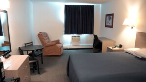 Une chambre d’hôtel comprenant un lit, un bureau, une chaise, une lampe de bureau, une fenêtre avec des rideaux et un tableau accroché au mur.