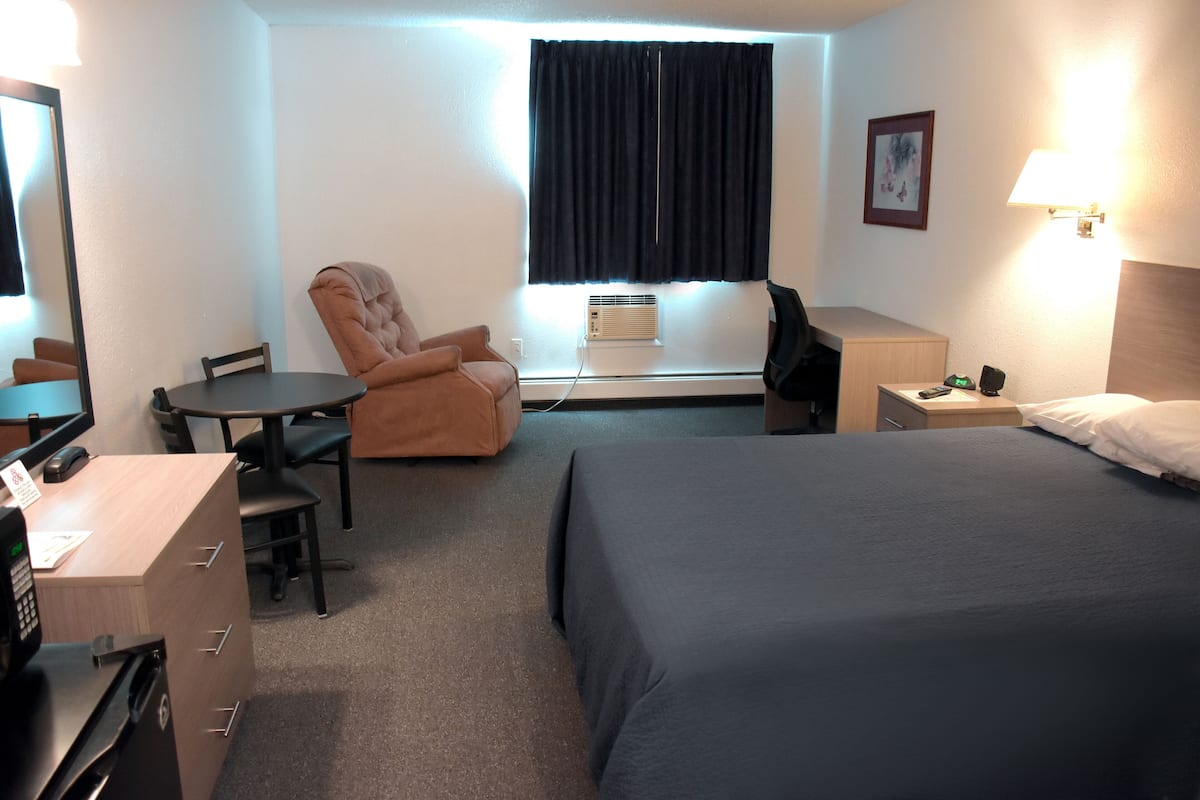 A hotel room with a bed, a desk, a chair, a desk lamp, a window with curtains, and a wall-mounted picture.