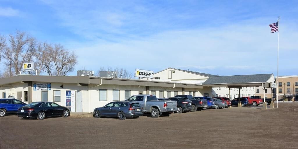 A building with a sign indicating it is a restaurant, multiple parked cars, and a flag.