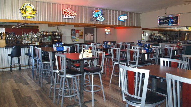 Un bar avec de nombreuses tables et chaises, des enseignes lumineuses de marques comme Coors Light et Bud Light, et une variété de bouteilles exposées sur des étagères.
