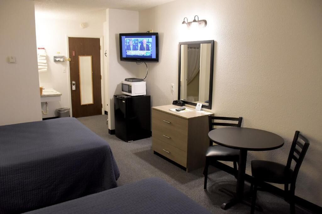 A hotel room with two beds, a desk with a chair, a television, a microwave, and a mirror.
