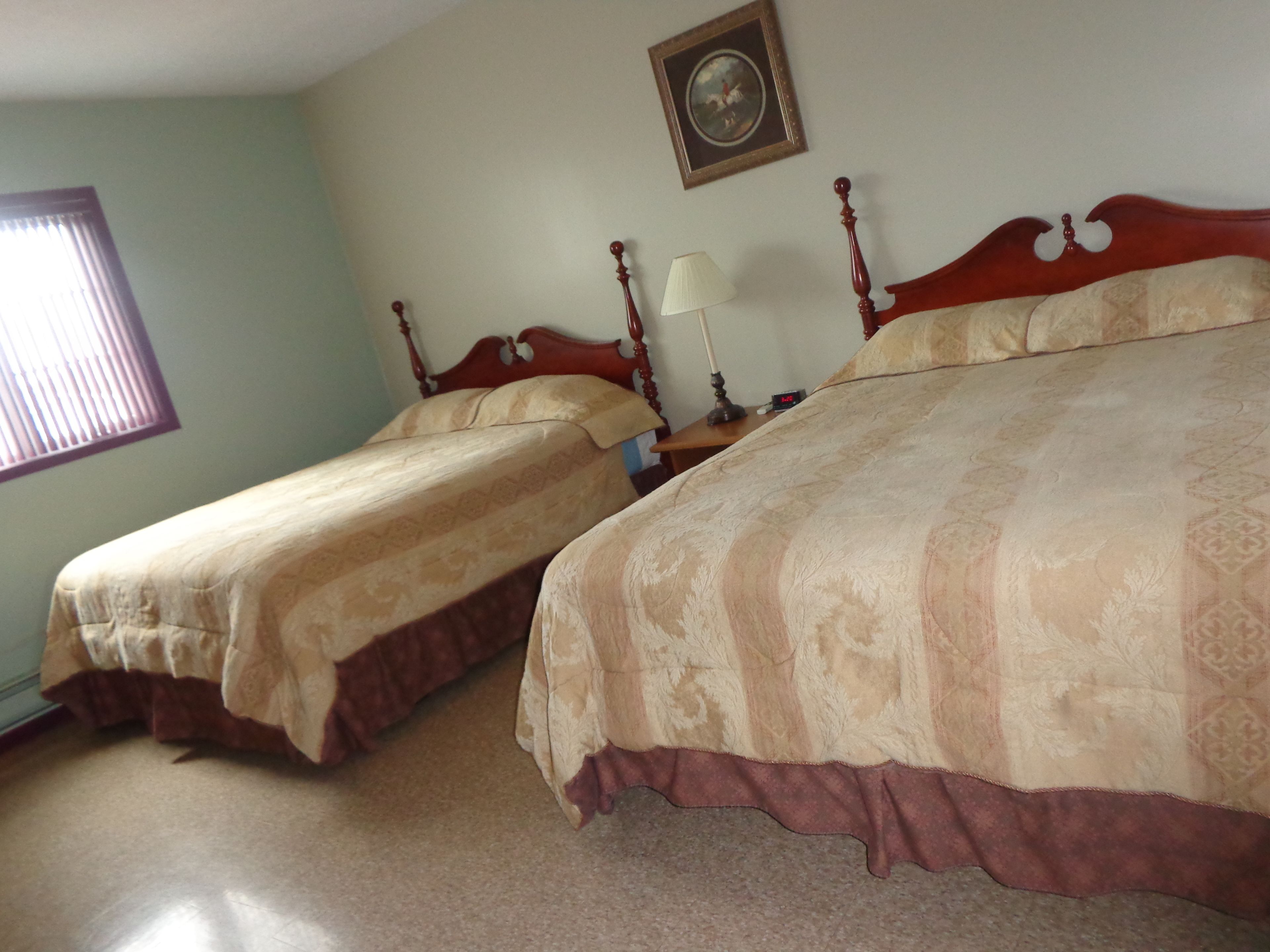 A bedroom with two single beds, a nightstand with a lamp, and a framed picture on the wall.