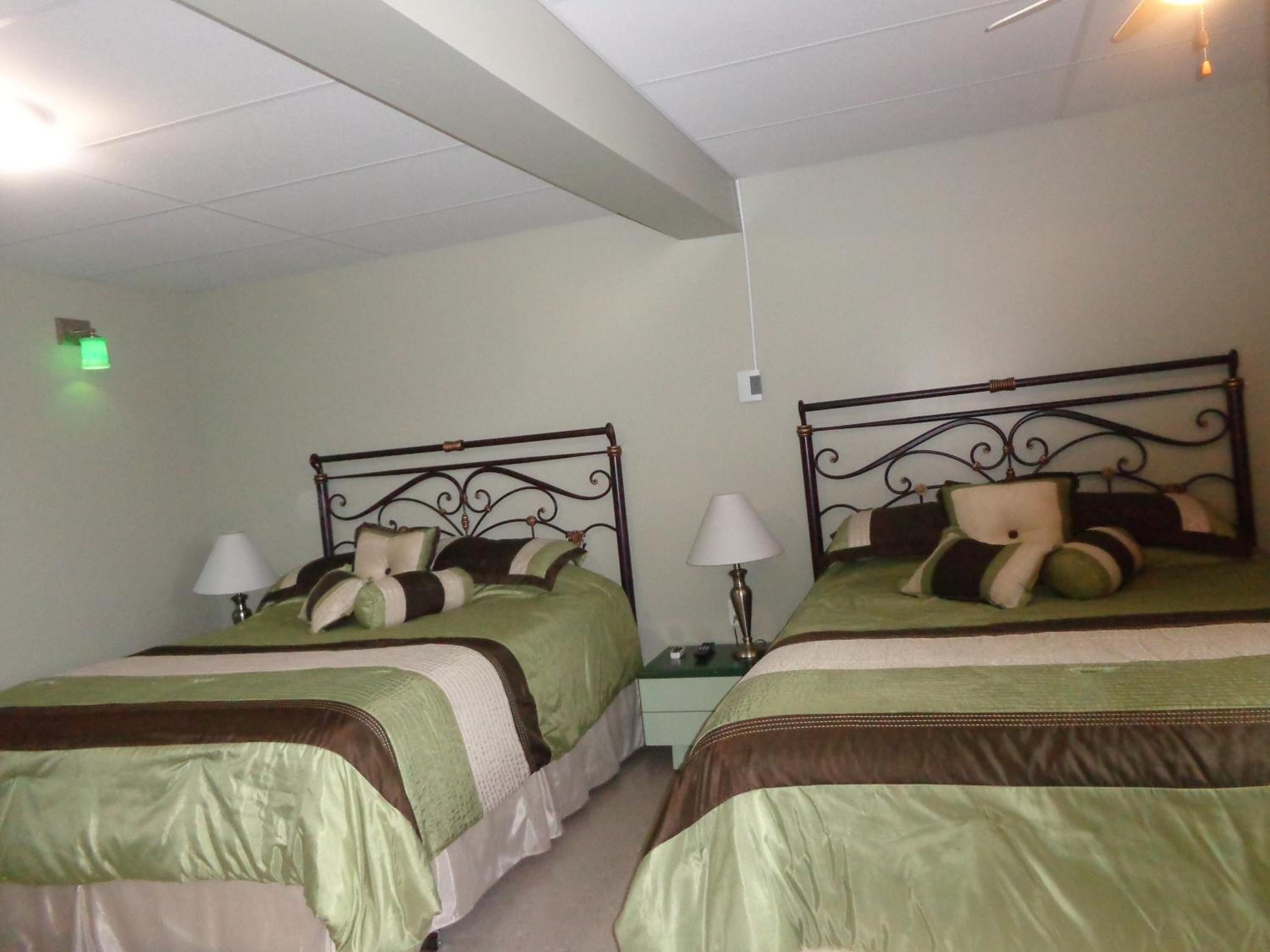 Una habitación con dos camas individuales, cada una con cabecero de metal, ropa de cama verde y una mesita de noche con lámpara.