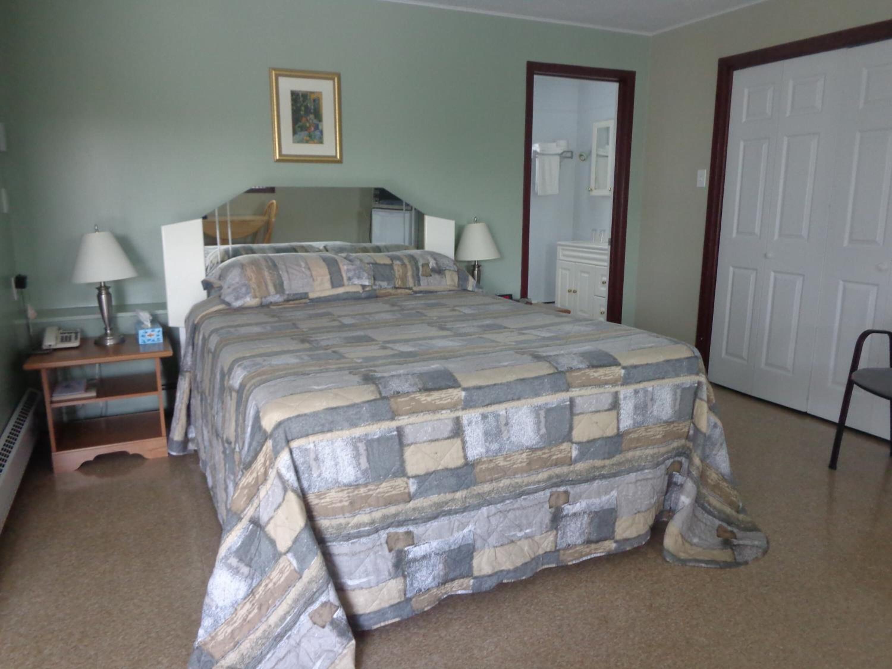 Een slaapkamer met een bed, nachtlampjes, een nachtkastje, een dressoir, een spiegel en een deur.