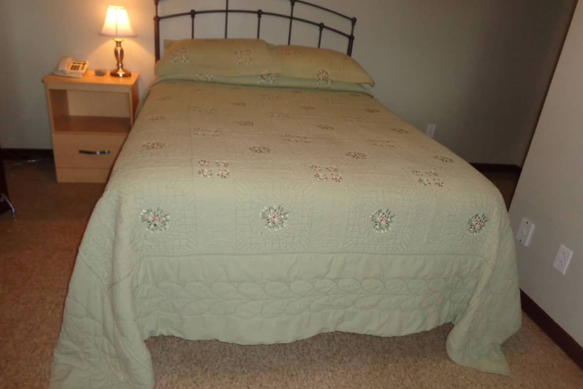 A neatly made bed with a floral quilt, a bedside lamp, and a nightstand with a phone.