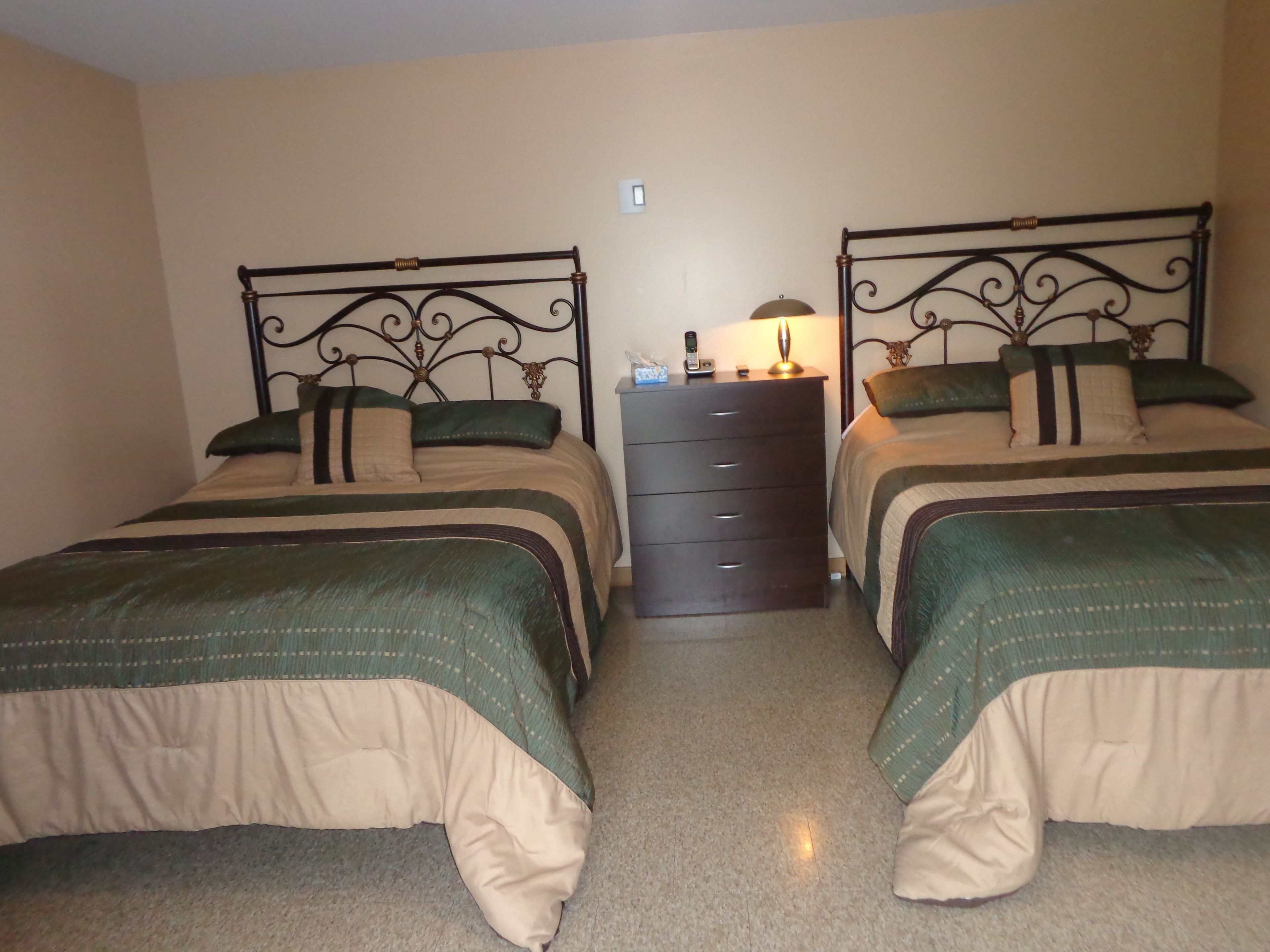 A room with two beds, each with a headboard, a dresser, and a nightstand with a lamp.