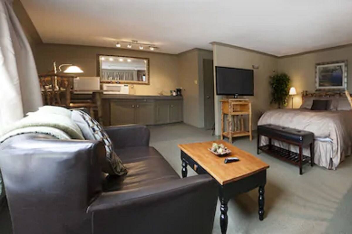 Uma sala moderna com sofá, mesa de centro e televisão. Há uma área de jantar com mesa e cadeiras, e um quarto com cama e mesa de cabeceira.