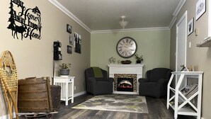 Una sala de estar con chimenea, dos sillones, piso de madera y un reloj de pared.