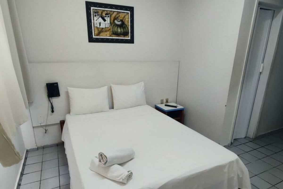 A hotel room with a bed, a nightstand, a telephone, and a painting on the wall.