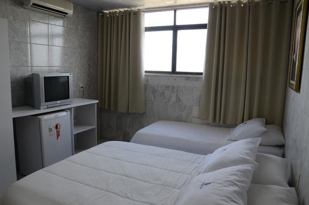 Quarto de hotel com duas camas, televisão, frigorífico e janela com cortinas.