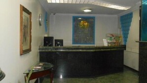 A reception area with a marble floor, a reception desk, a framed picture on the wall, a potted plant, and a blue wall decoration. - Titao Plaza Hotel (Campina Grande)