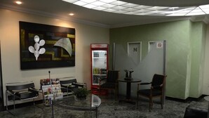 A lobby with a glass table, black chairs, a red vending machine, and a wall-mounted artwork. - Titao Plaza Hotel (Campina Grande)