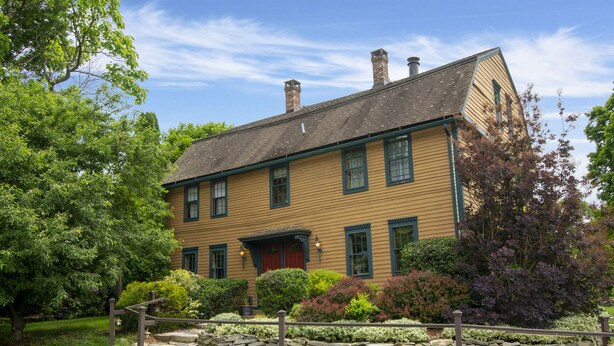 A two-story house with a stone foundation, green shutters, and a red door. - Captain Grant's 1754 (Preston)
