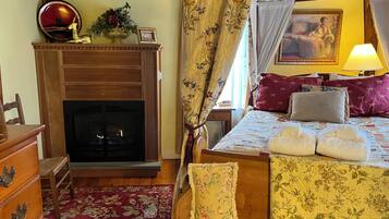 A cozy room with a fireplace, a bed with floral bedding, a wooden dresser, and a red rug.