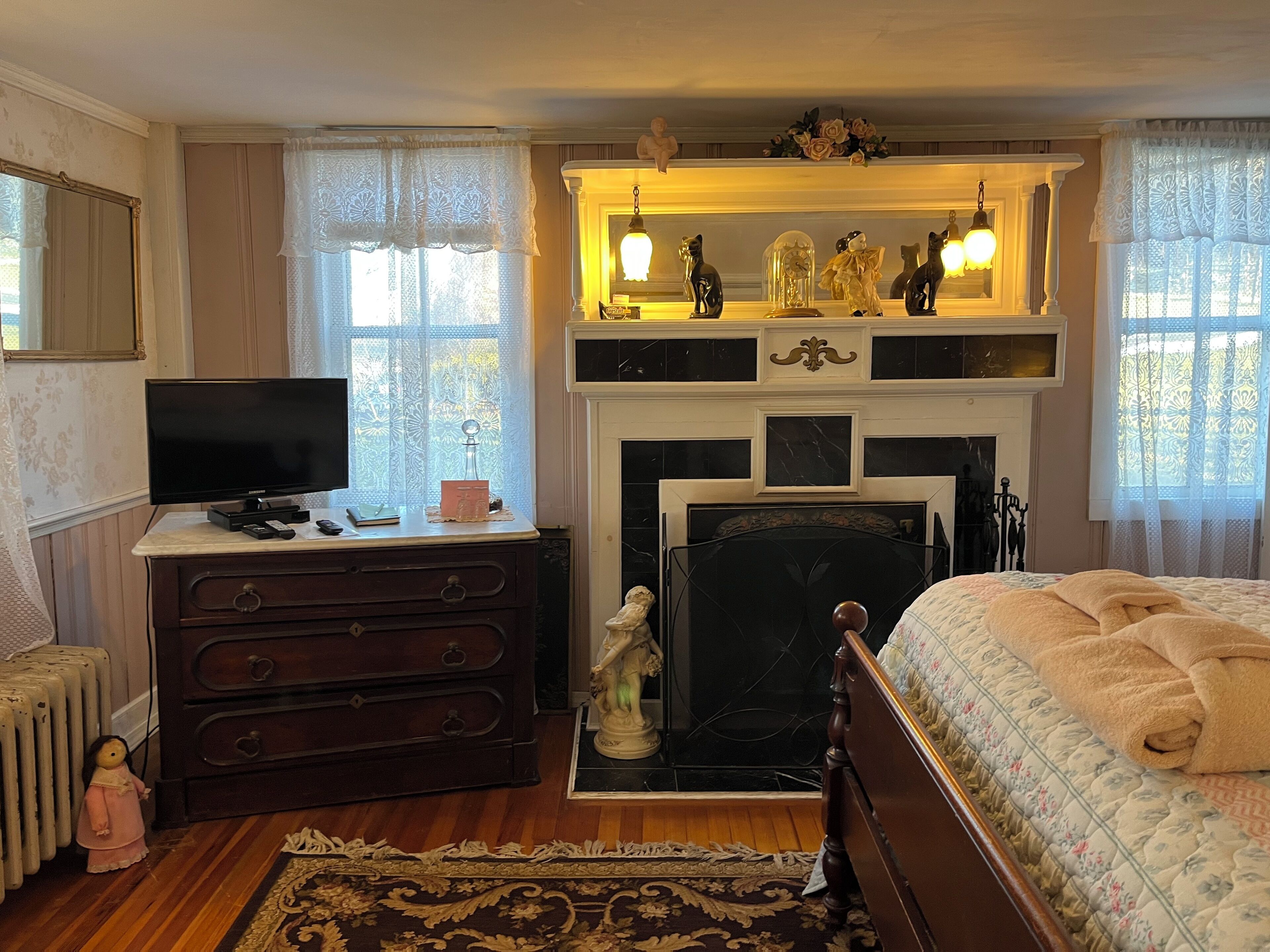 A bedroom with a bed, dresser, television, fireplace, and decorative items.