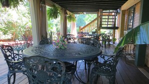 A covered outdoor patio with a round table and chairs, surrounded by potted plants and a wooden railing. - Captain Grant's 1754 (Preston)
