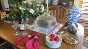 A dining table set with a cake, wine glasses, a bottle of wine, a vase of flowers, and a blue and white ceramic jug. - Captain Grant's 1754 (Preston)