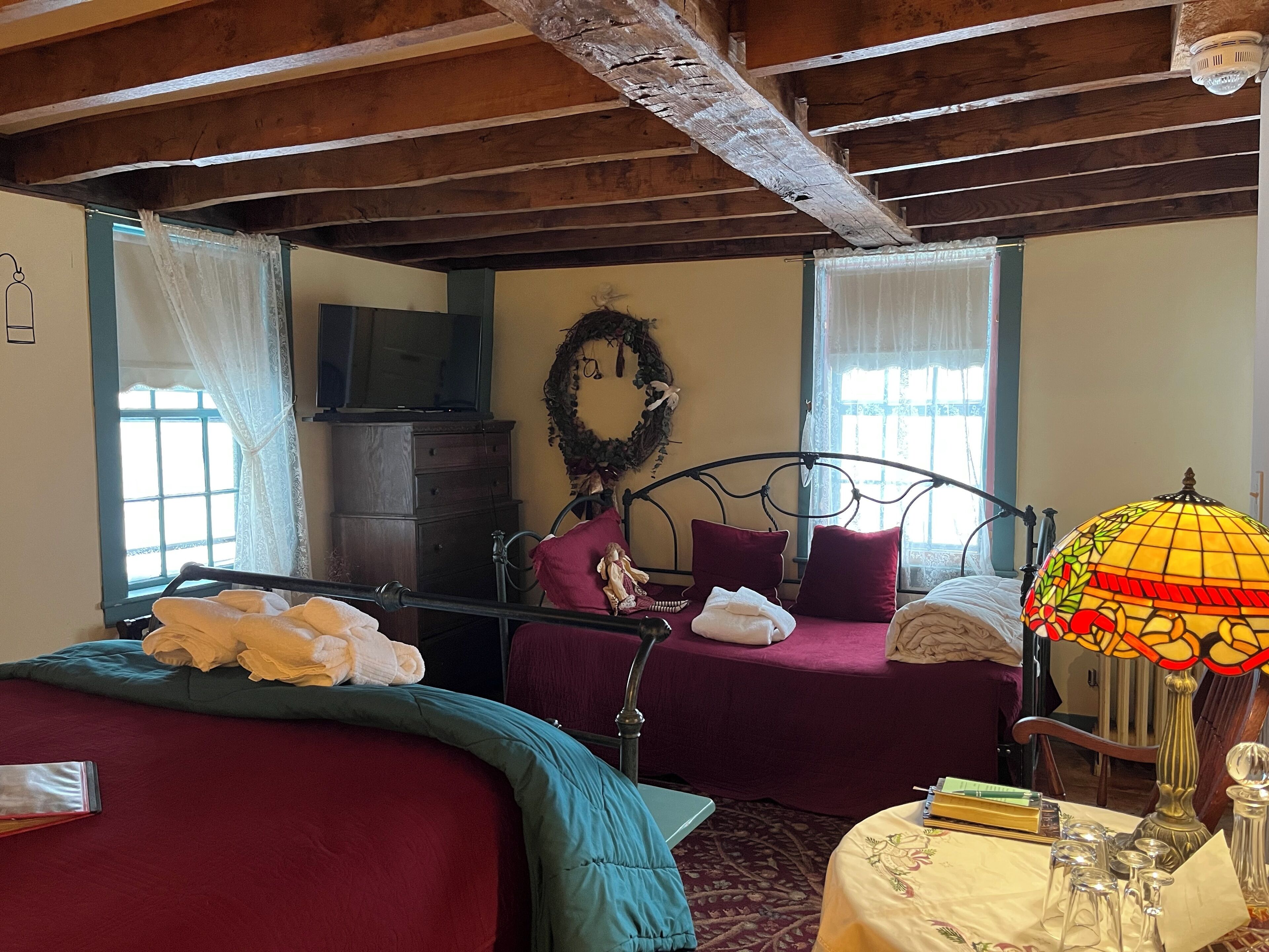 Una habitación con dos camas, techo de madera, televisor y una lámpara decorativa.