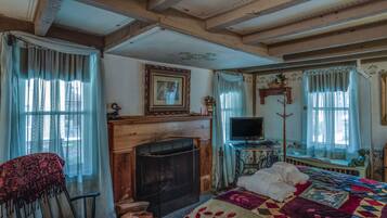 Een gezellige kamer met een open haard, een bed met quilt, een stoel en een televisie op een standaard.