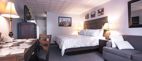 A hotel room with a bed, a desk, a chair, a sofa, and a lamp.