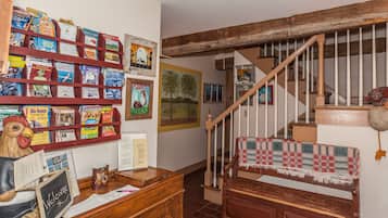 Un interior rústico con una escalera de madera, una estantería llena de libros y revistas, y un letrero de bienvenida sobre un escritorio.