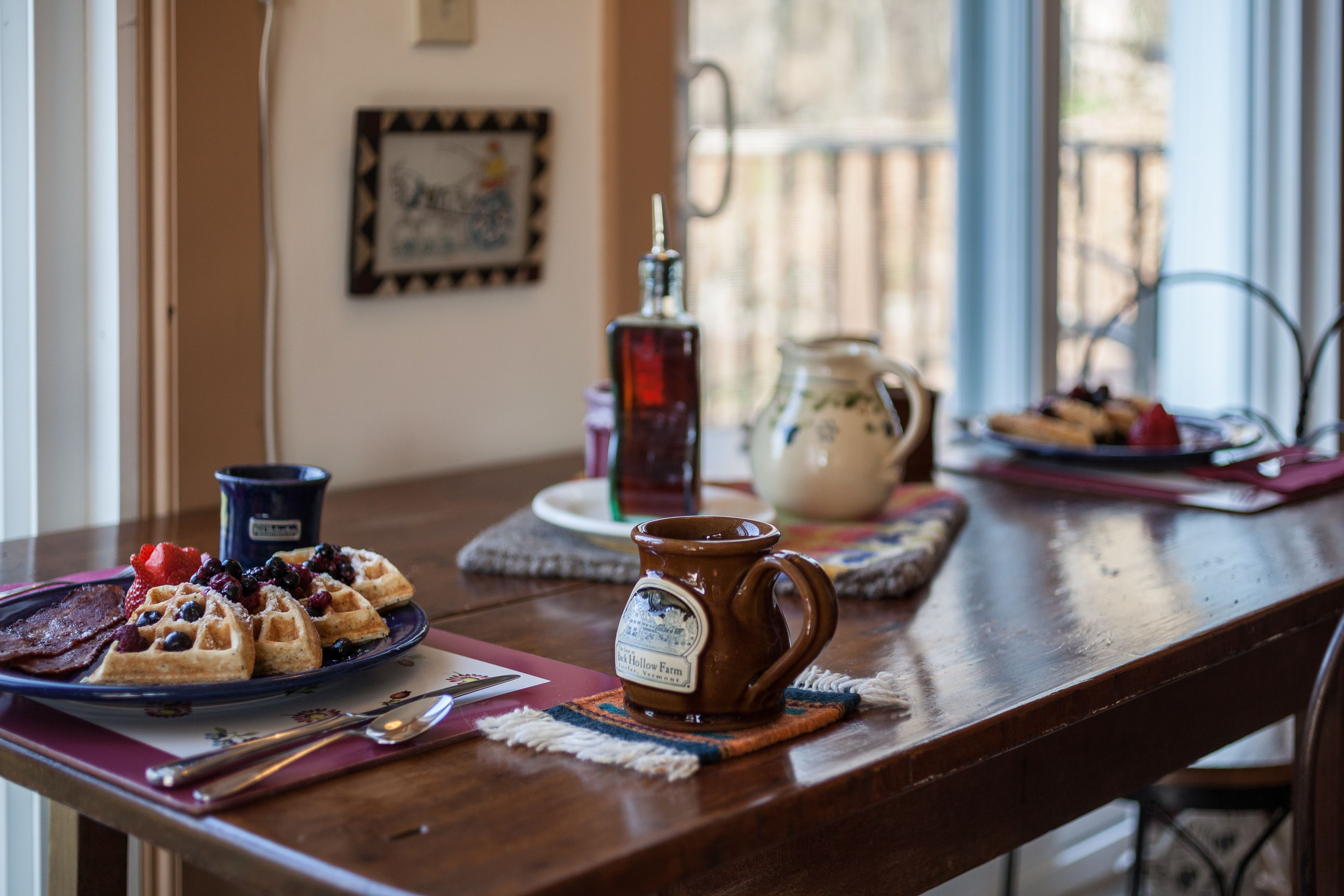 Una mesa de desayuno con waffles, jarabe y una taza.