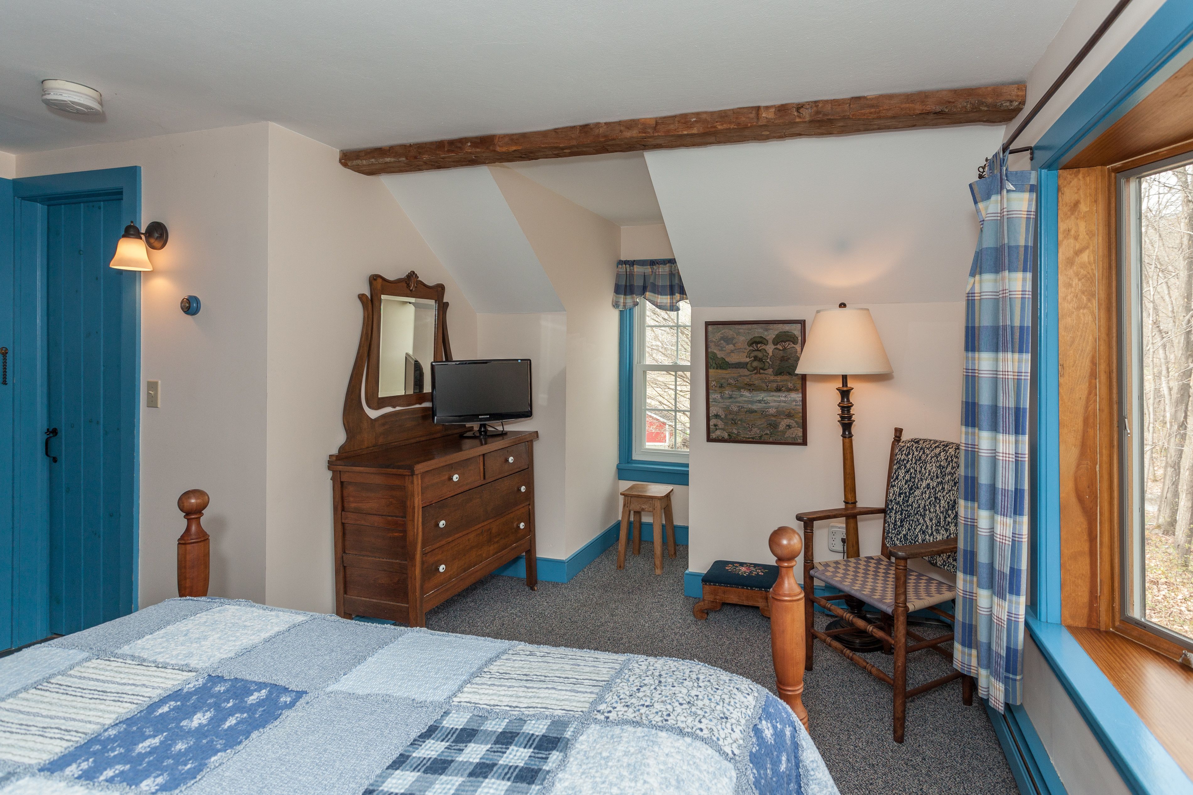 A bedroom with a bed, dresser, television, chair, and a window with curtains.