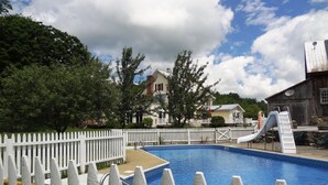 A swimming pool with a white picket fence, a slide, and a building in the background. - The Inn at Buck Hollow Farm (Fairfax)