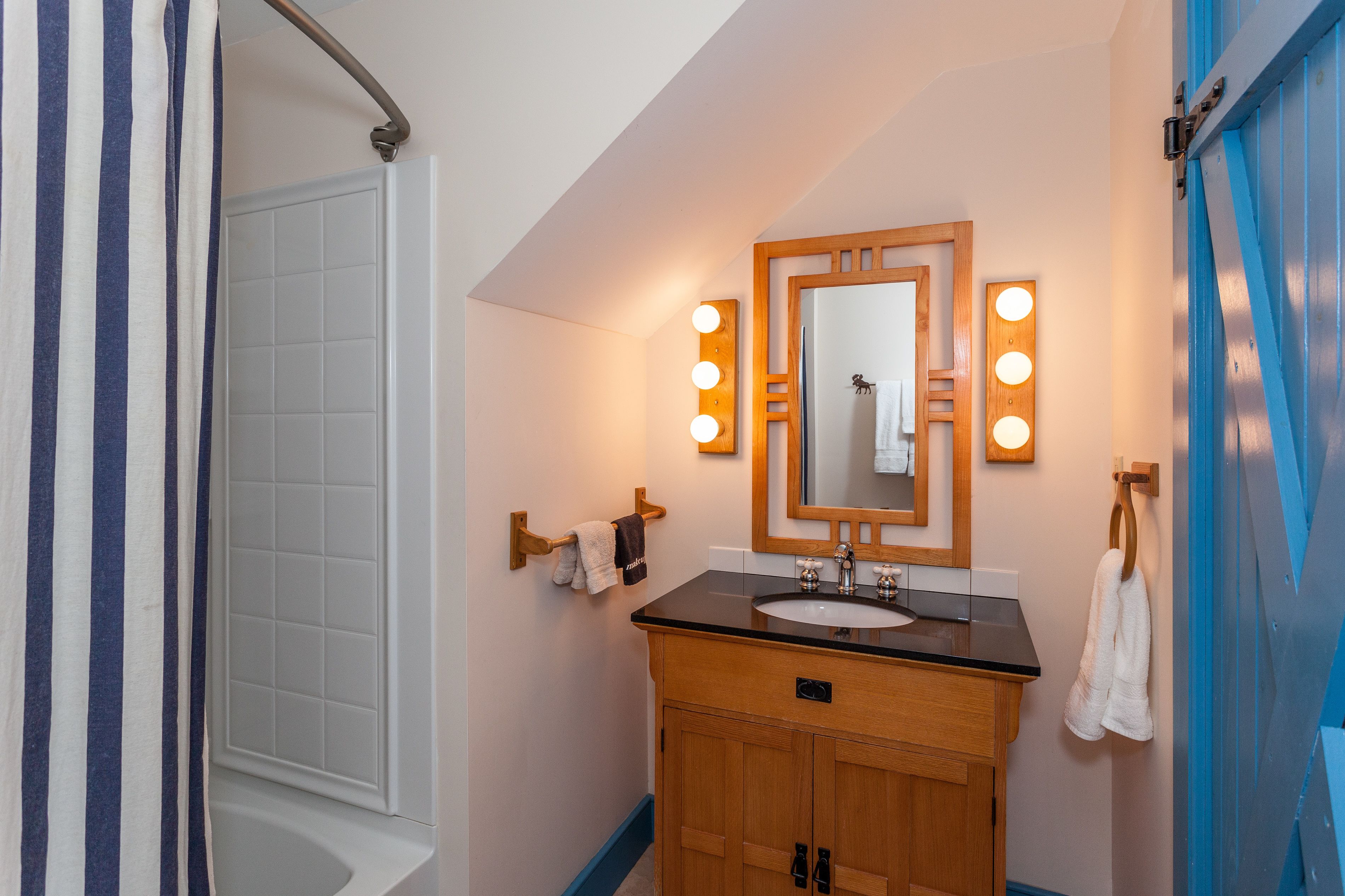 A bathroom with a wooden vanity, a large mirror with lights, a white sink, and a shower curtain.