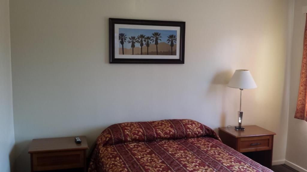 Ein Hotelzimmer mit Bett, Nachttisch, Lampe und einem gerahmten Bild an der Wand.