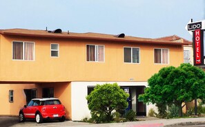 A two-story hotel with a red car parked in the driveway, a sign indicating it's a Lido Hotel, and a number '6523' on the building.
