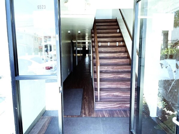 Un escalier menant à un couloir dont l’entrée est une porte vitrée.