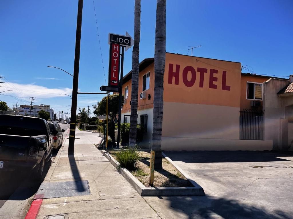 A hotel with a prominent 'HOTEL' sign on the building, a parking area with cars, and a clear sky.