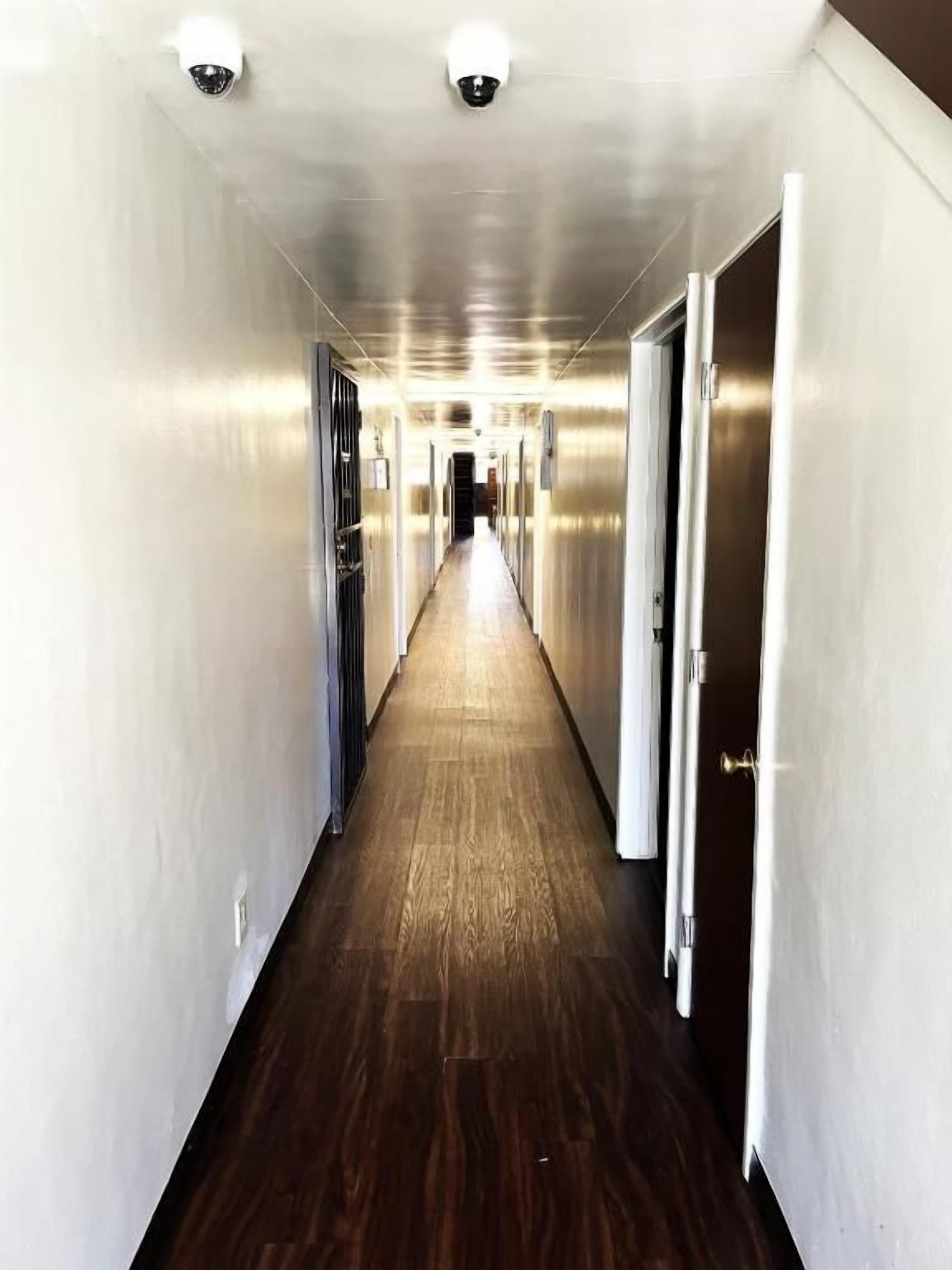 A hallway with a wooden floor and metallic walls, leading to a door at the end.