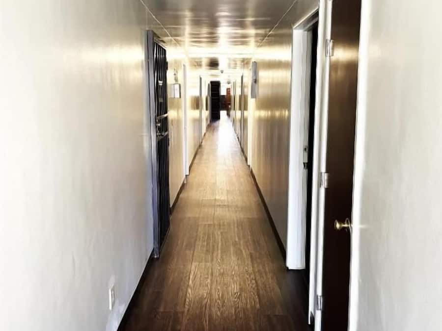 Un pasillo con piso de madera y paredes metálicas, que conduce a una puerta al final.