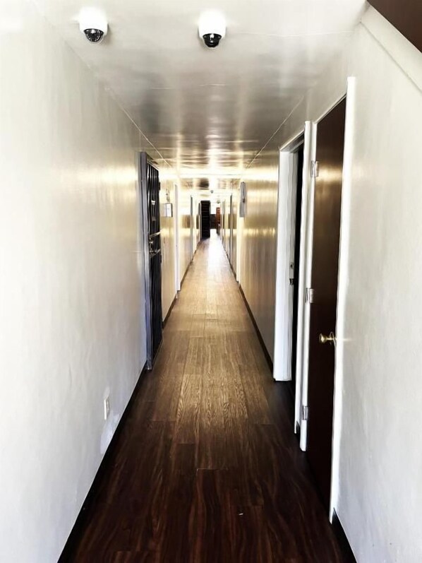 A hallway with a wooden floor and metallic walls, leading to a door at the end.