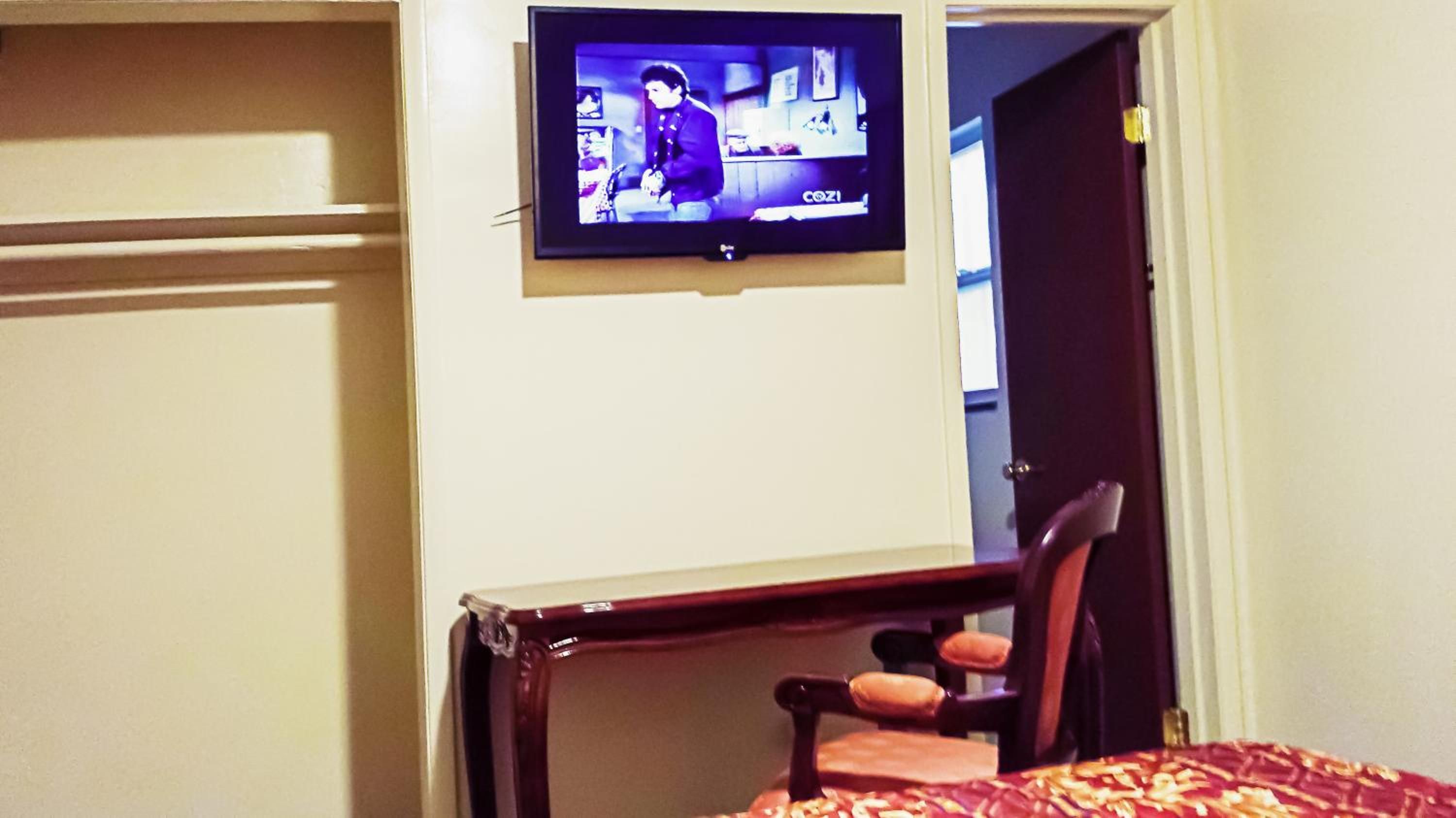 A hotel room with a television mounted on the wall, a wooden chair, and a bed with a patterned bedspread.