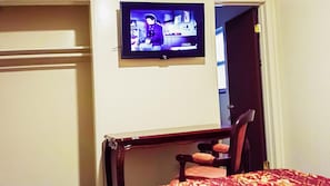 A hotel room with a television mounted on the wall, a wooden chair, and a bed with a patterned bedspread. - Lido Hotel (Huntington Park)