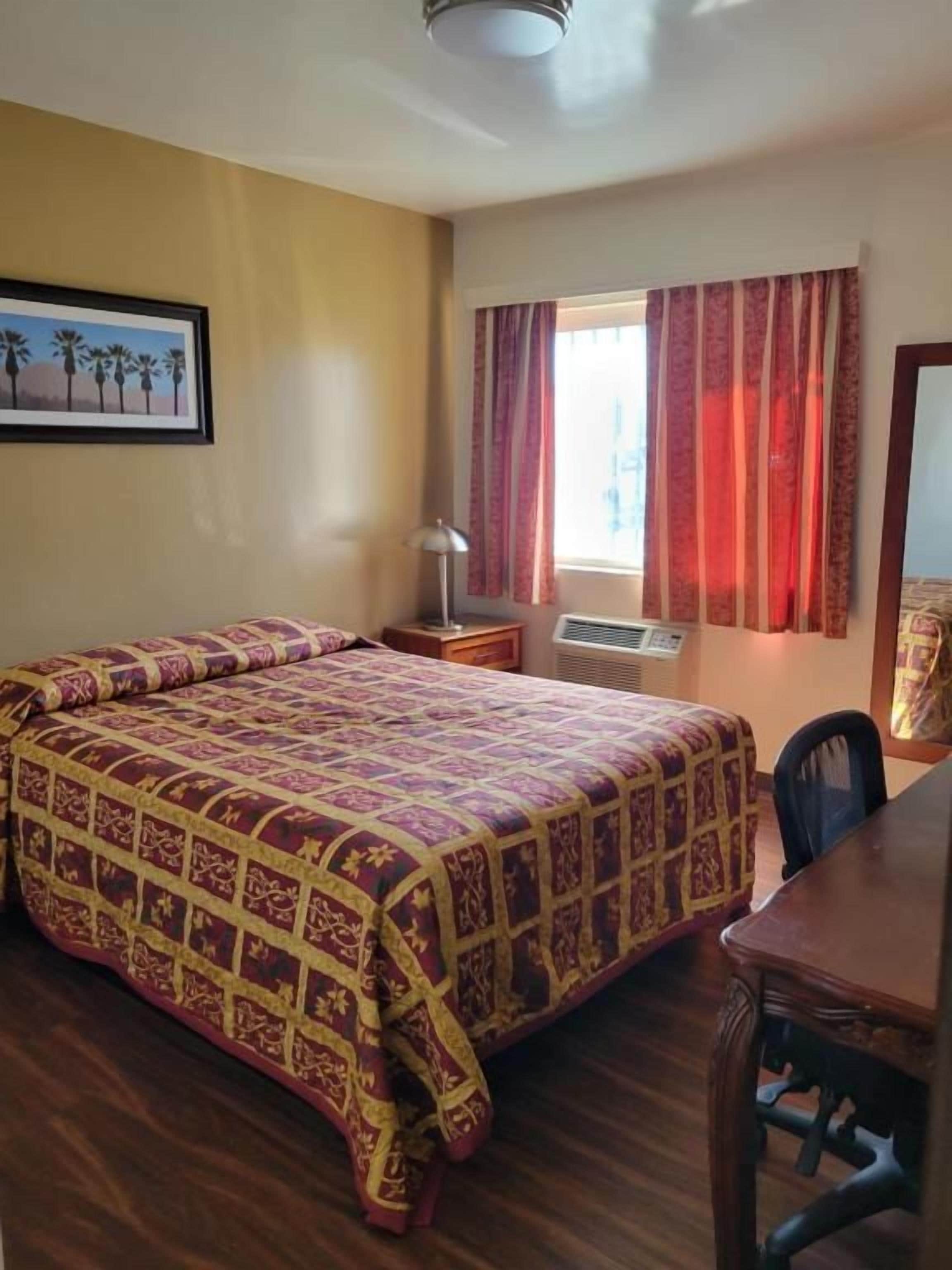 Une chambre d’hôtel avec un lit, un bureau, une chaise, une fenêtre avec des rideaux et un tableau au mur.