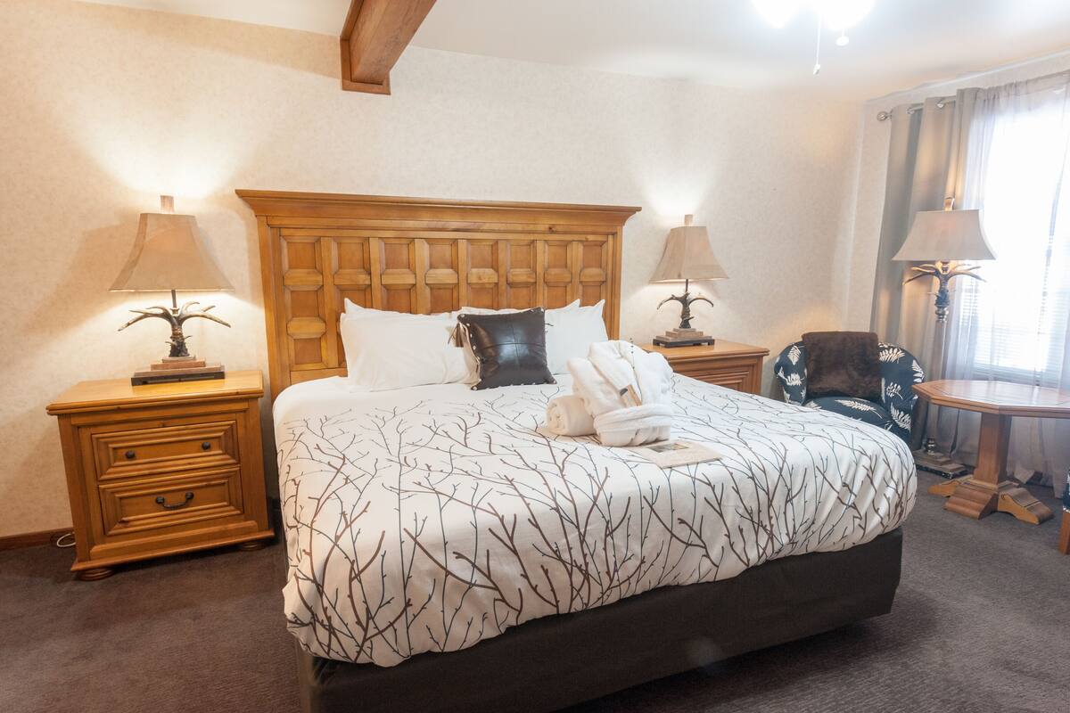 A neatly made bed with a patterned bedspread, two bedside tables with lamps, a wooden nightstand, and a chair.