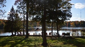 A lakeside setting with a dock, chairs, and a table under a tree. - Heather Lodge (Minden Hills)