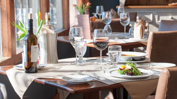 A dining table set with wine glasses, plates, and a bottle of wine, with a window view in the background. - Heather Lodge (Minden Hills)