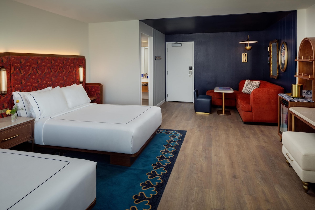 A hotel room with a large bed, a red sofa, a small table, and a desk with a lamp.