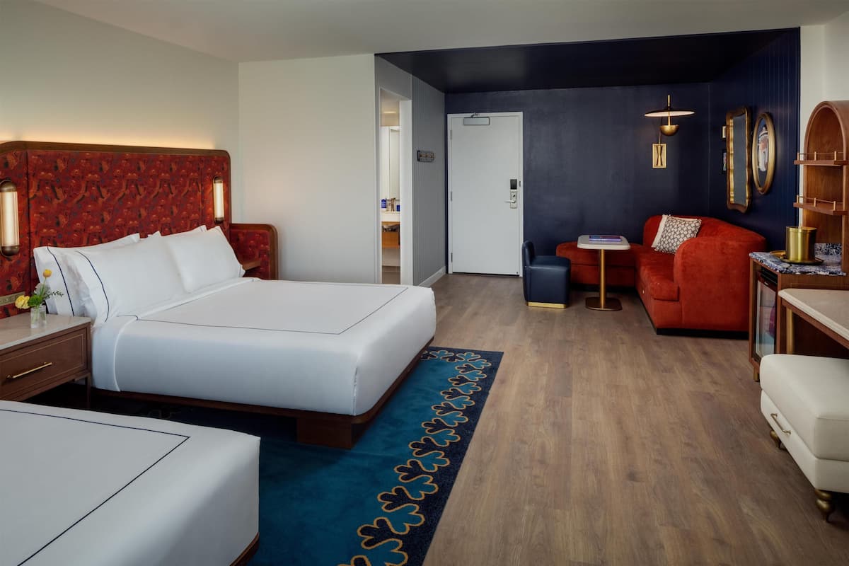 A hotel room with a large bed, a red sofa, a small table, and a desk with a lamp.