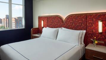 Une chambre d’hôtel avec un grand lit, une table de chevet, une commode, une fenêtre donnant sur la ville et une tête de lit à motifs.