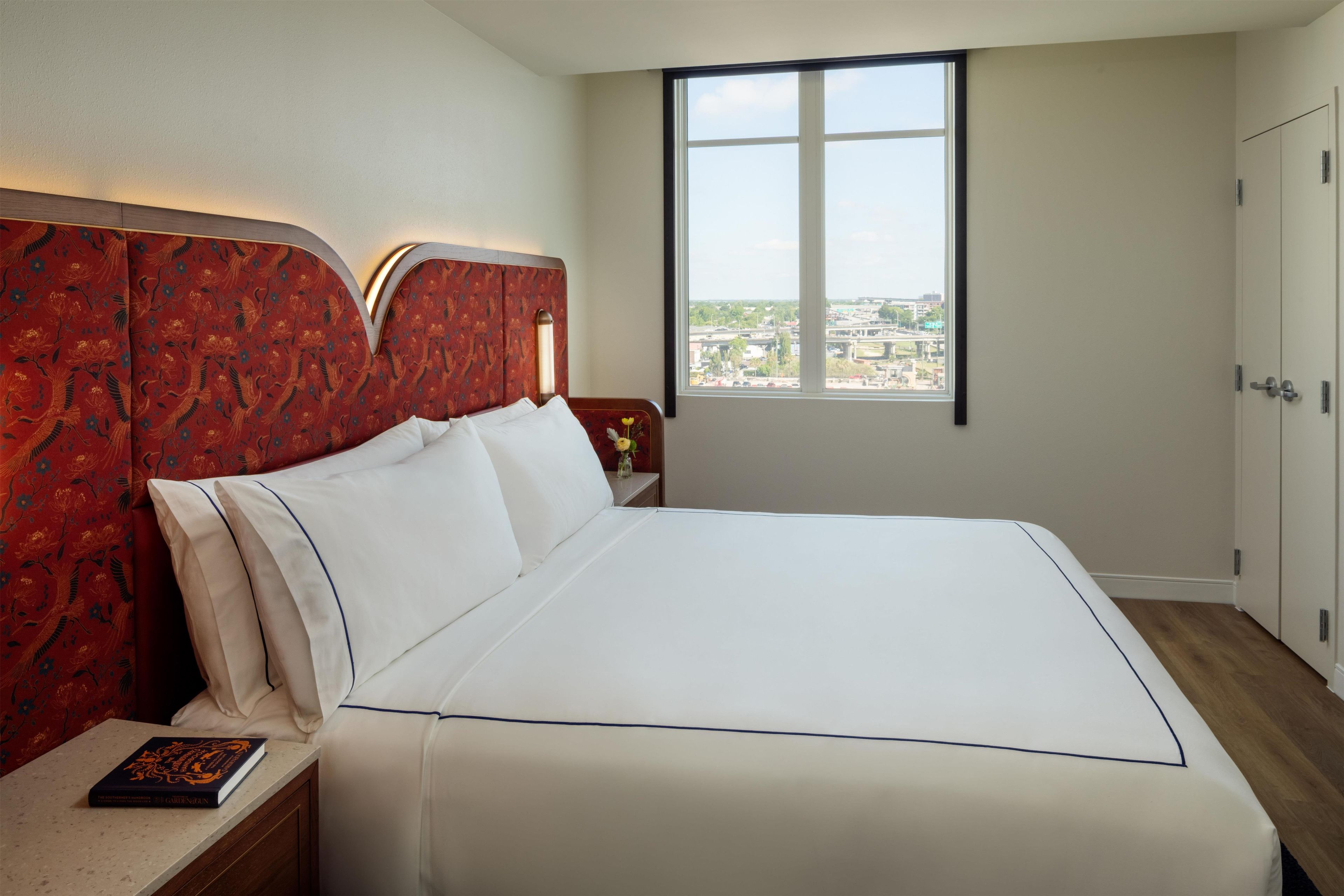 A hotel room with a large bed, a nightstand, a window with a city view, and a wardrobe.